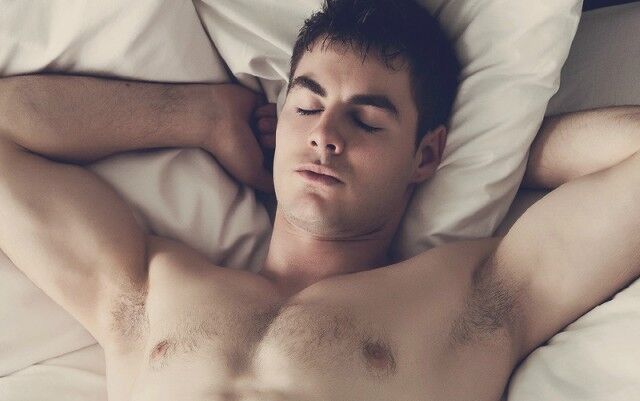 A person rests on a light-colored pillow with eyes closed and arms bent behind the head.