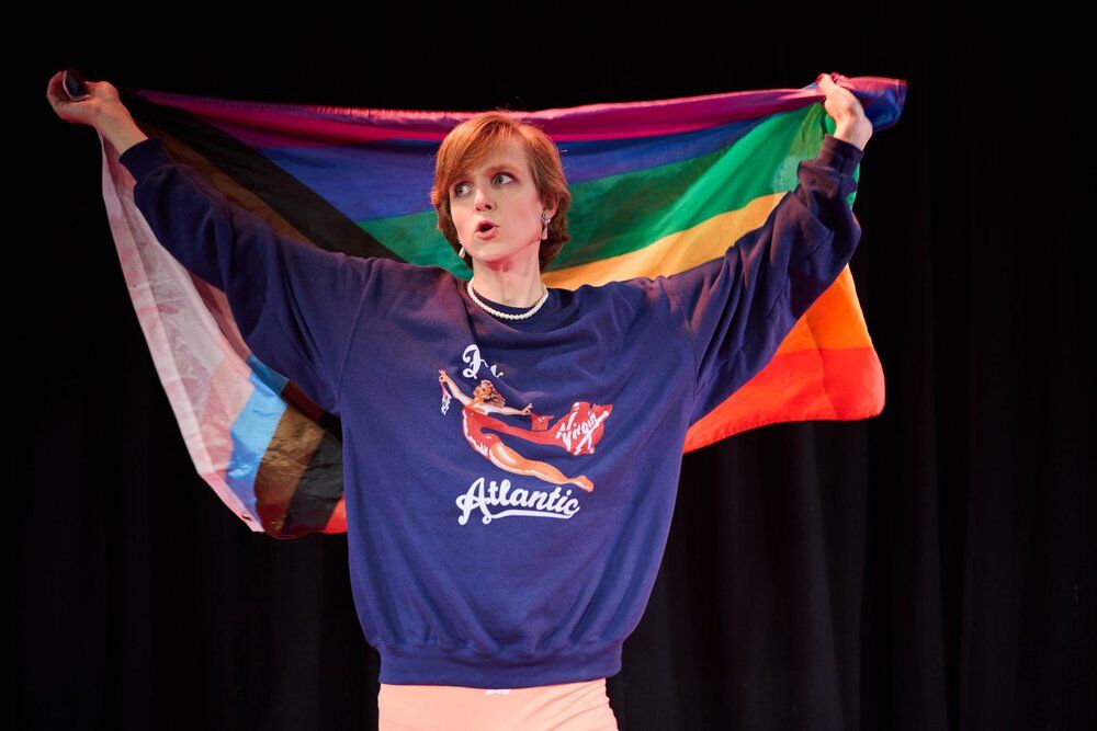 Linus Karp as Princess Diana holding a Progress Pride flag onstage