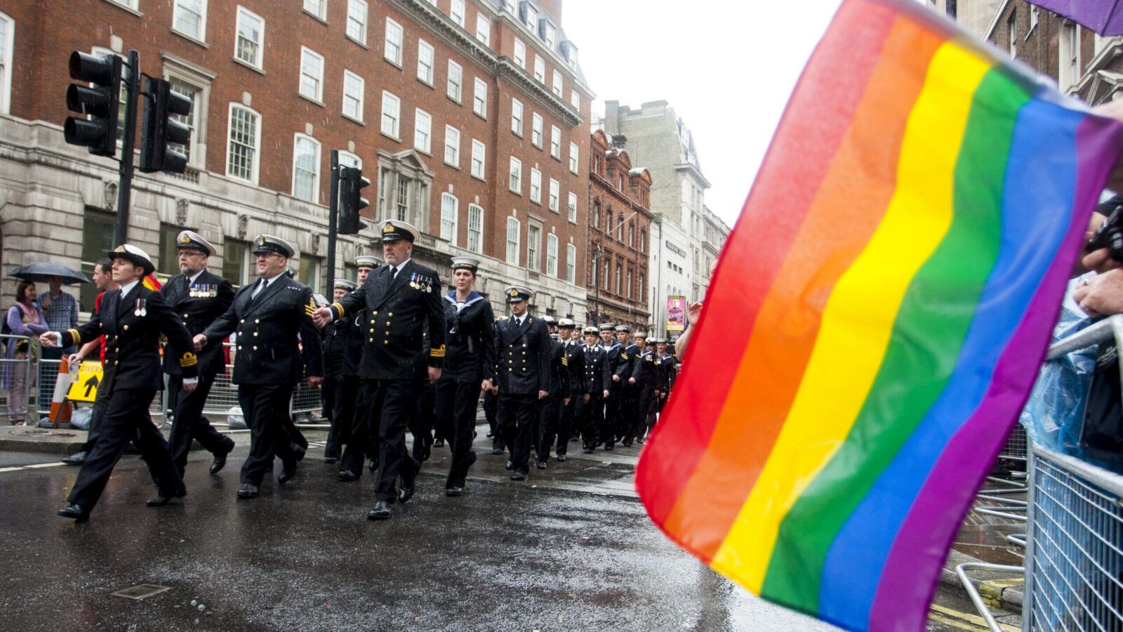 Uniformed military personnel march past a rainbow flag at Pride in London.